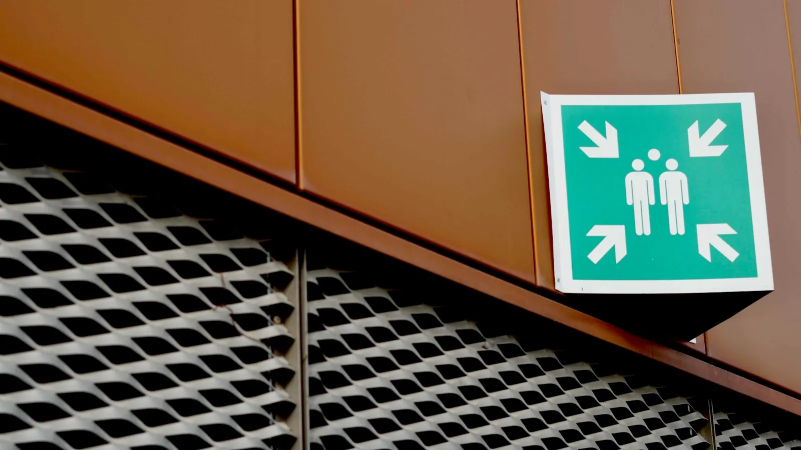 Green emergency assembly point sign fixed to the side of a building