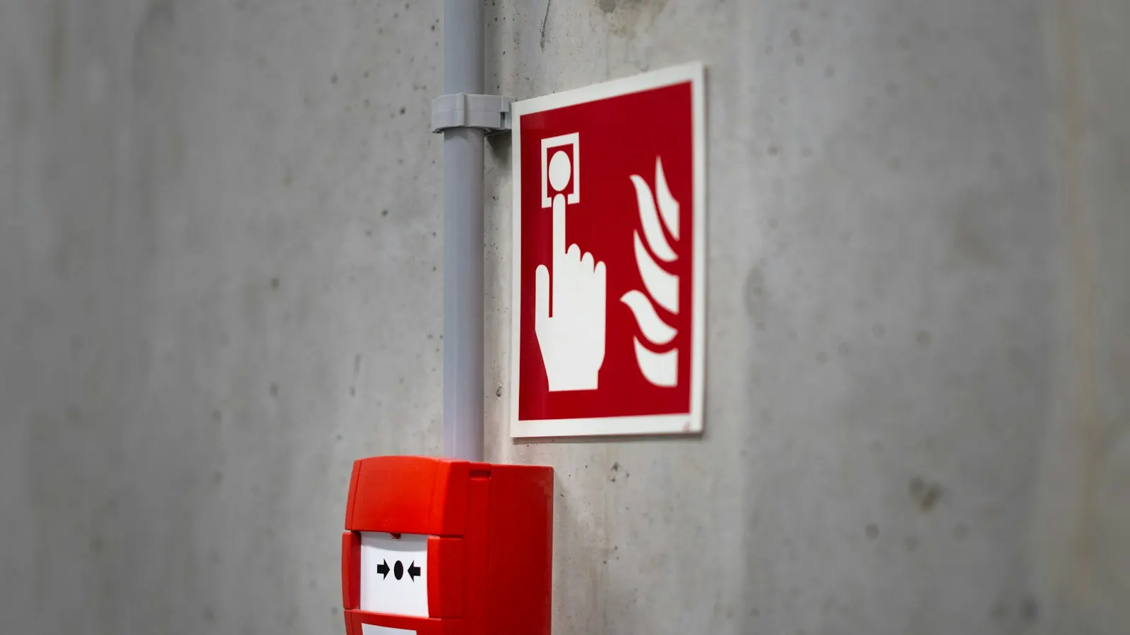 Wireless fire alarm call point mounted on a concrete wall beside a fire alarm pictogram sign