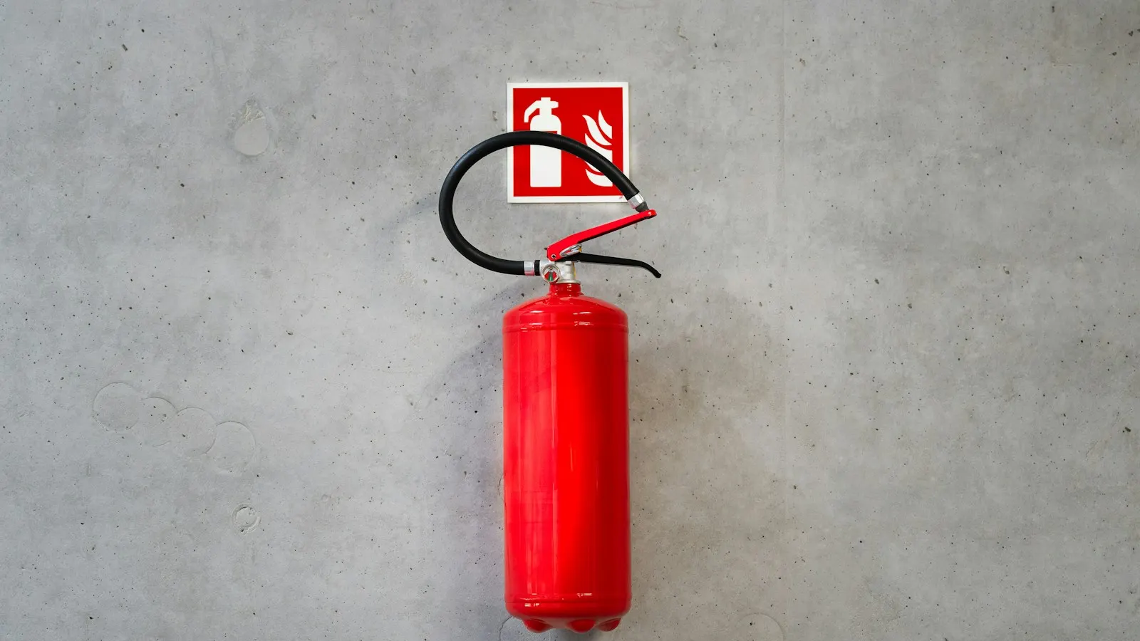 Red fire extinguisher mounted on a bare concrete wall below its identification sign