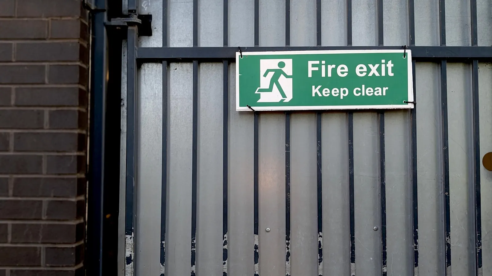 Green fire exit and keep clear sign fixed to a construction site gate