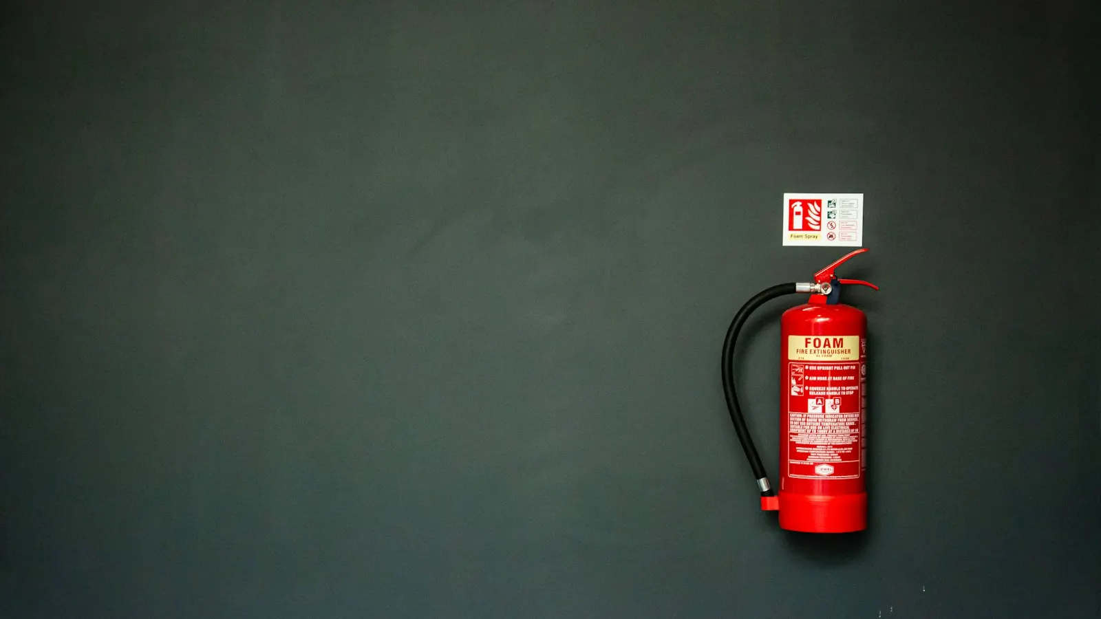 Foam fire extinguisher mounted on a dark green wall with its service label visible