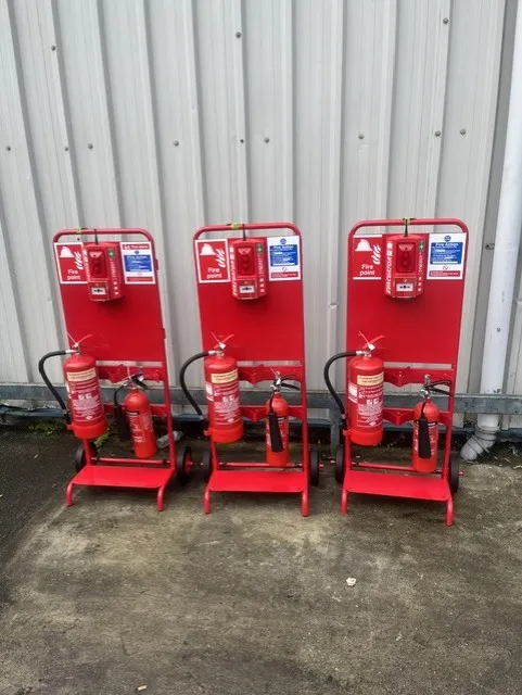 Three radio linked fire trolleys lined up against a corrugated metal wall